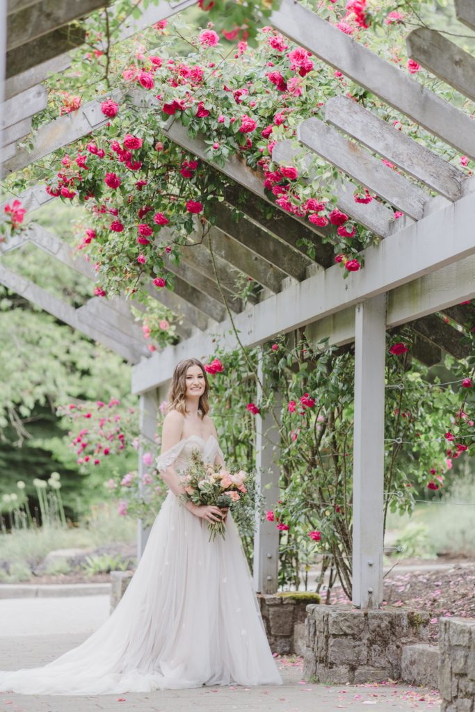 Bride in whimsical wedding dress in rose garden trellis