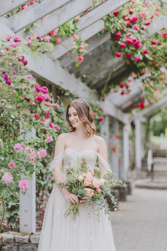 Bride in whimsical wedding dress in rose garden trellis